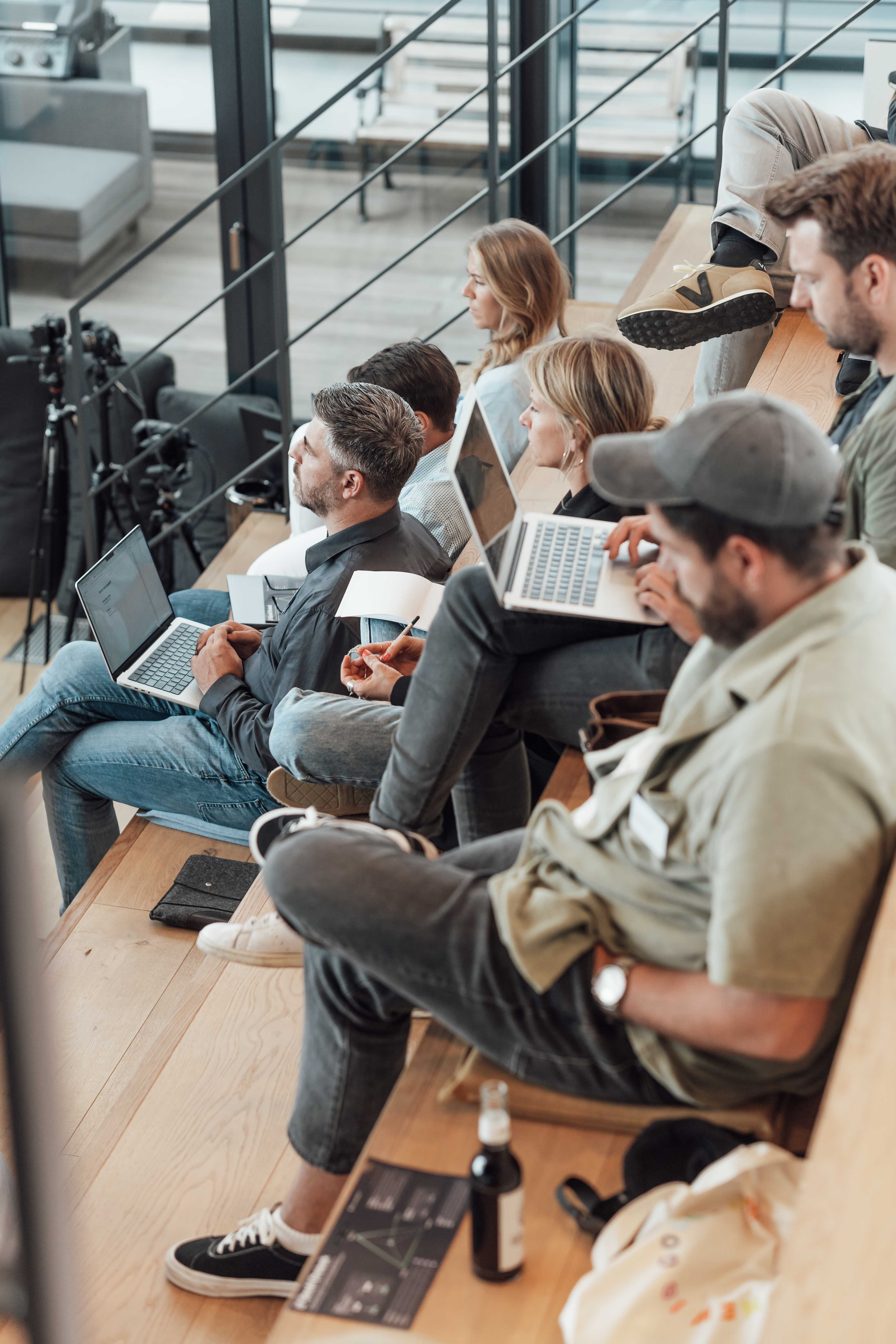 Teilnehmende sitzen mit Laptops auf einer Tribüne beim Blackboat AI Experience Day.