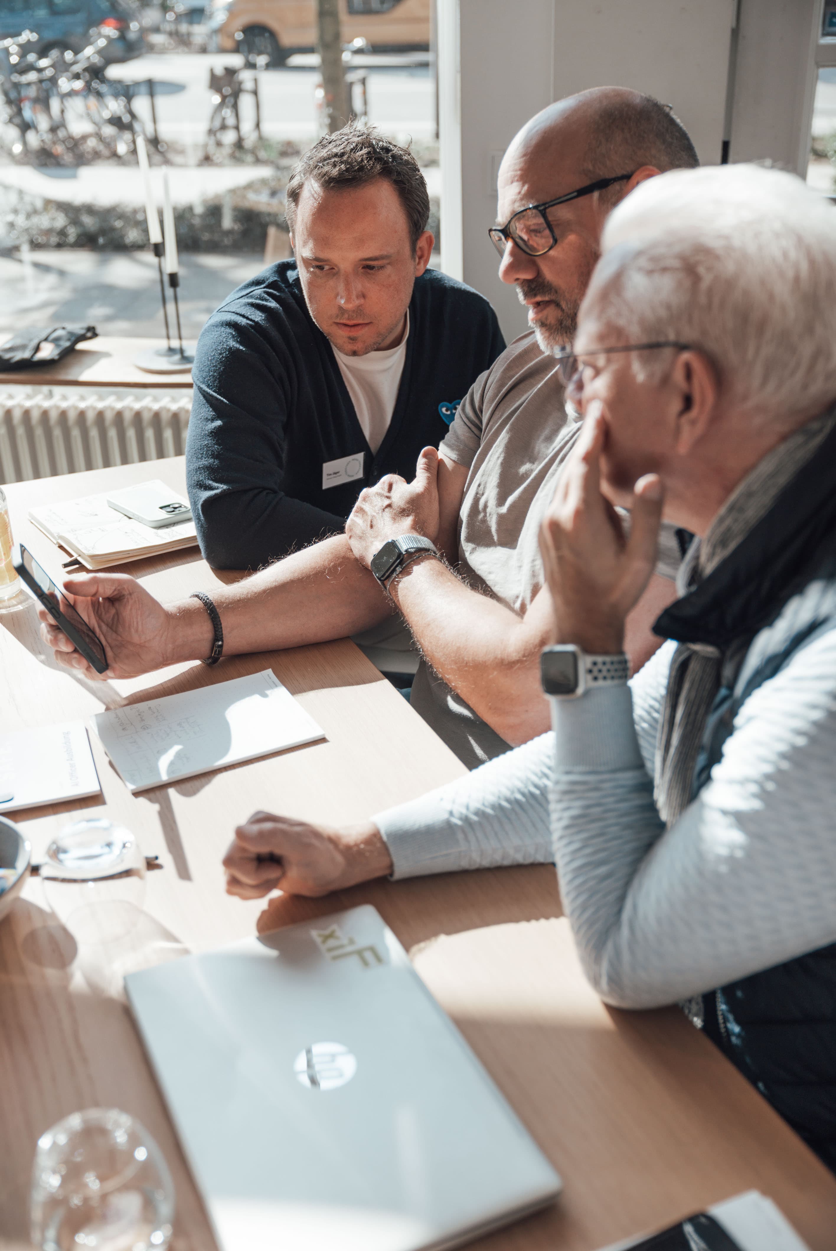 Drei Personen in einer Workshop-Situation schauen gemeinsam auf ein Smartphone